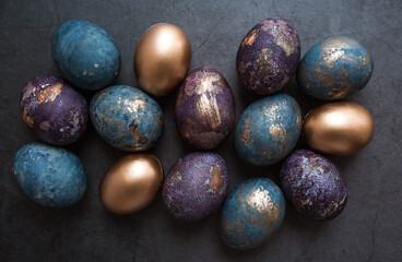 Purple, blue and golden eggs on a dark concrete background. The purple hue trend of 2022 is very peri. Easter card with a copy of the place for the text. Natural dye karkade tea. Top view.
