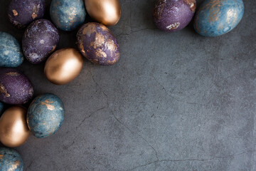 Purple, blue and golden eggs on a dark concrete background. The purple hue trend of 2022 is very peri. Easter card with a copy of the place for the text. Natural dye karkade tea. Top view.