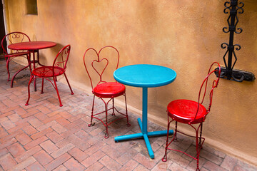 Pretty colourful outdoors metal chairs and tables set on brick terrace, with stucco wall in the background, Santa Fe, New Mexico, USA