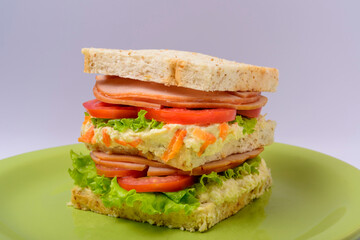 Big sandwich with smoked ham, with lettuce and tomato on green plate. Fast food.