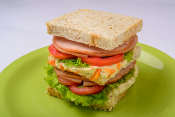 Big sandwich with smoked ham, with lettuce and tomato on green plate. Fast food.