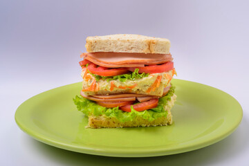 Big sandwich with smoked ham, with lettuce and tomato on green plate. Fast food.