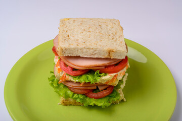 Big sandwich with smoked ham, with lettuce and tomato on green plate. Fast food.