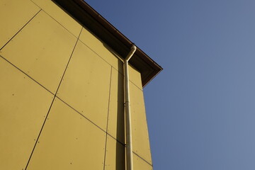 Upper right corner of dark yellow house wall with rain gutter, German 70s design, clear blue sky, use: copy space, texture, background (horizontal), Kaiserslautern, RLP, Germany