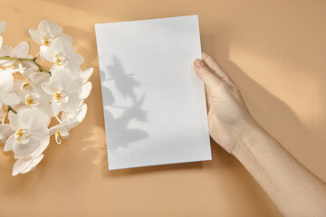 Hands are holding an empty white A5 form on a beige background. Layout top view