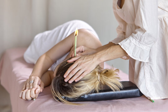 Beautiful woman receiving ear candle treatment. Therapist performing an ear wax treatment on a patient using candling. Naked woman receiving ear candle treatment from masseur