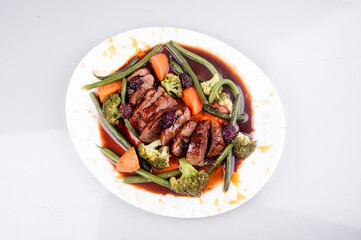 duck magret with vegetables on white plate isolated top view