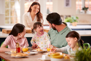 Family With Down Syndrome Daughter Sitting Around Table At Home Eating Breakfast