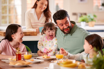 Father Making Funny Face As Family With Down Syndrome Daughter Eat Breakfast At Home