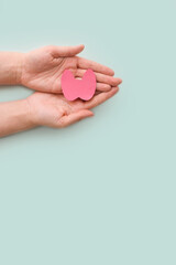 World Thyroid Day. Women's hands hold a paper form of the thyroid gland on a blue background. Problems with thyroid. Polycystic disease. World cancer day. copy space. vertically.