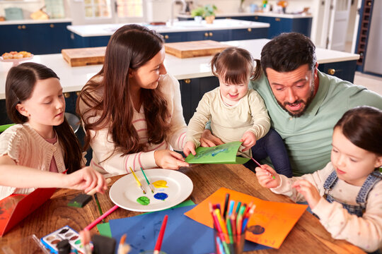 Family With Down Syndrome Daughter Sitting Around Table At Home Doing Craft Together