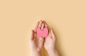 Fototapeta na wymiar World Thyroid Day. Women's hands hold a paper form of the thyroid gland on beige background. Problems with thyroid. Polycystic disease. World cancer day. banner