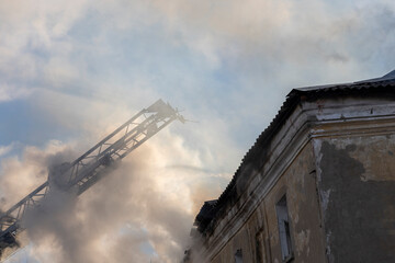 Firefighter works on boom of fire engine. Fireman on sky background. Burning old building in the historic center..Rescuers on a retractable ladder in the smoke.