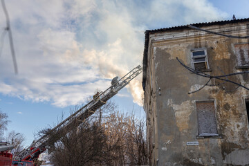 Firefighter works on boom of fire engine. Fireman on sky background. Burning old building in the historic center..Rescuers on a retractable ladder in the smoke.