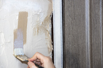 The builder applies soil to the wall. A painter paints the slope of a doorway with a brush, makes...