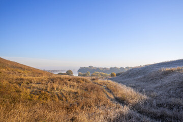 Autumn landscape in the early morning. Fog-covered expanses through which the first rays of the rising sun pass. Trees and hills in the fog. Dawn on a cold autumn morning.