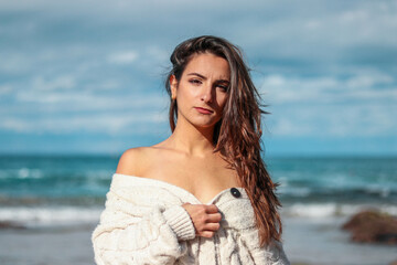 Beautiful and brunette woman looking to the camera on the beach in a sweater