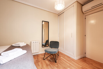 Bedroom with bed, built-in wardrobe, air conditioning unit and chair upholstered in blue velvet.