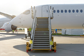 Civil jet aircraft with ladder stairs and airport and other plane on background.