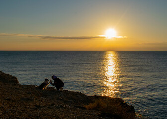 Chico con su perro en la playa mirando el amanecer
