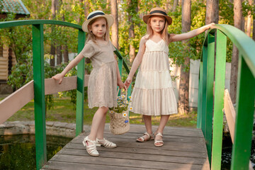 Preteen girls posing on wooden bridge over small pond in country estate on summer day