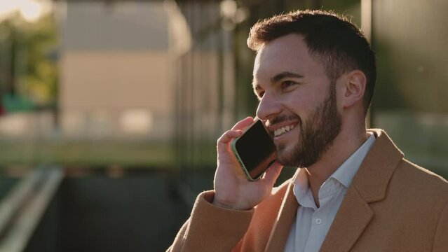 Handsome man in beige coat talking on mobile outdoors
