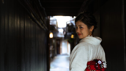 Fototapeta premium 京都、祇園の小さな路地で和服を着て微笑み振り返る日本人女性。バストアップショット