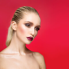 Fototapeta premium Closeup portrait of young female model with perfect makeup with bare shoulders, isolated on a red background.