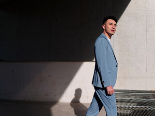 Confident businessman, portrait of handsome Chinese young man in light blue suit smiling and walking into sunlight, side view.