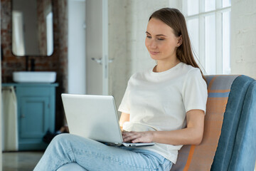 Beautiful young woman working on a laptop in a home interior. Freelancer A modern business woman uses a laptop for remote work or online shopping.