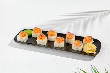 Maki sushi with salmon top on black plate. Sushi roll with philadelphia cheese inside and salmon tartare outside. Maki roll in minimal concept. Summer menu for japanese restaurant.