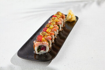 Modern asian food - maki sushi with salmon and berries on black plate on white concrete background. Sushi roll with tuna inside and salmon, mango and berries outside. Fusion sushi menu.