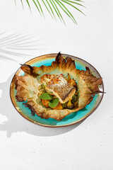 Baked halibut fillet with vegetables in parchment. Fish dish - roasted halibut with potato, broccoli and cauliflower. Food menu in minimal concept. Baked white fish on white concrete background.
