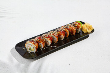 Modern asian food - sushi roll with eel on black plate on white concrete background. Canada maki with eel outside, avocado, cheese and shrimp inside. Unagi maki. Fusion sushi menu.