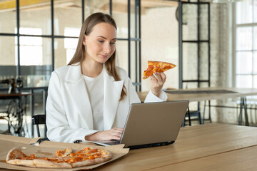 Business woman working an office desk with a laptop and having a lunch break with a tasty pizza. 