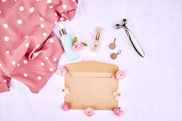 Elegant vivid spring envelope mock up with pink flowers, accessories, massager, cosmetic gift on fabric white background. 8 of March concept