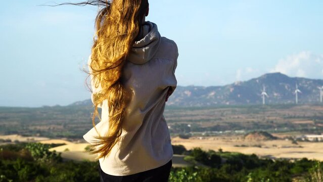 Casual woman with very long and healthy red hair looking towards Vietnam landscape on windy day