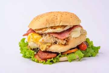 Big hamburger sandwich with smoked ham, cheese, eggs, sausage, bacon, lettuce and tomato on white background.