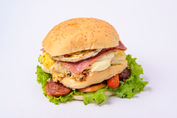 Big hamburger sandwich with smoked ham, cheese, eggs, sausage, bacon, lettuce and tomato on white background.