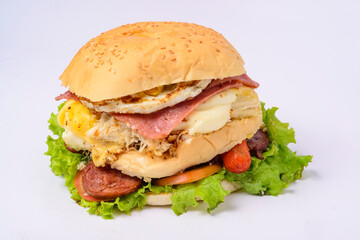 Big hamburger sandwich with smoked ham, cheese, eggs, sausage, bacon, lettuce and tomato on white background.