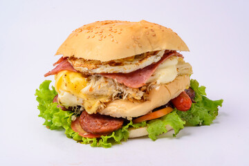 Big hamburger sandwich with smoked ham, cheese, eggs, sausage, bacon, lettuce and tomato on white background.