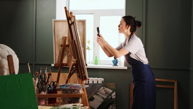 Art studio - young woman takes pictures of her painting on her phone