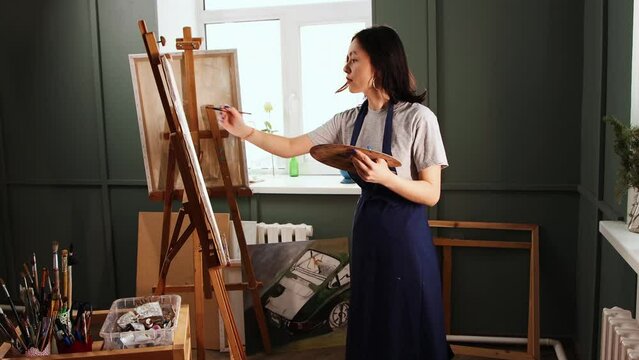 Art studio - young woman mixing colors on palette and ties up her hair