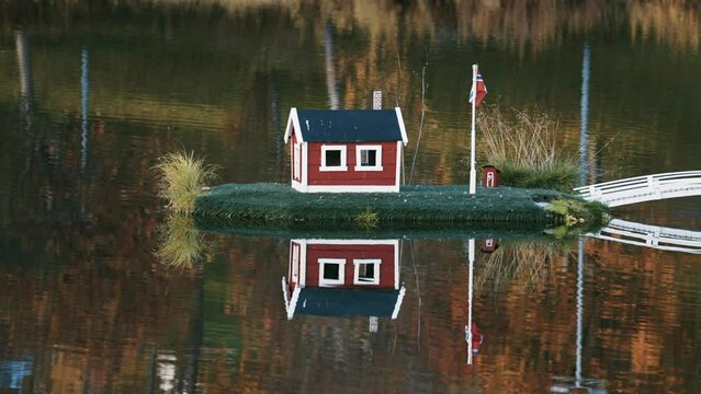 An idyllic scene in the town park in Sorreisa, Norway. Miniature houses with Norwegian flags in the middle of the lake reflected in the mirrorlike still water. Autumn foliage in the background.