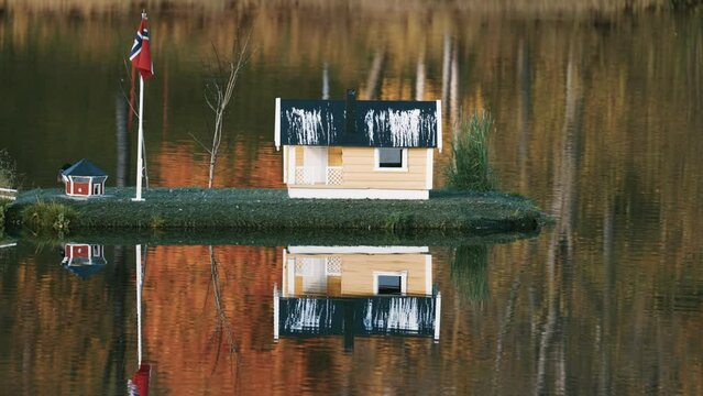 An idyllic scene in the town park in Sorreisa, Norway. Miniature houses with Norwegian flags in the middle of the lake. Autumn foliage reflected in the mirrorlike still water.