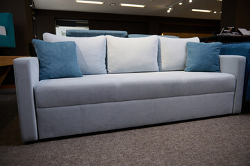 Beautiful minimalist stylish light gray settee with blue cushions, displayed on sale in the furniture store showroom. Living room furnishing with stylish modern comfortable upholstered furniture.