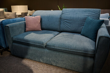 Furniture store showroom interior. Stylish blue sofa with pink pillows in the showroom of upholstered furniture. Furniture store with sofas and couches on display for sale, copy space.