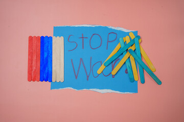 Small wooden pieces lined up with the images of the Russian and Ukrainian flags messed up with the text stop war in the center placed on a pink background. No war, stop war, russian aggression.