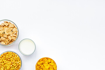 Various corn cereals in bowls and milk on white background top view copyspace
