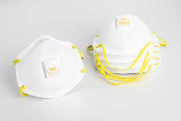 Isolated N95 facemask with yellow straps beside stack of facemasks on white background